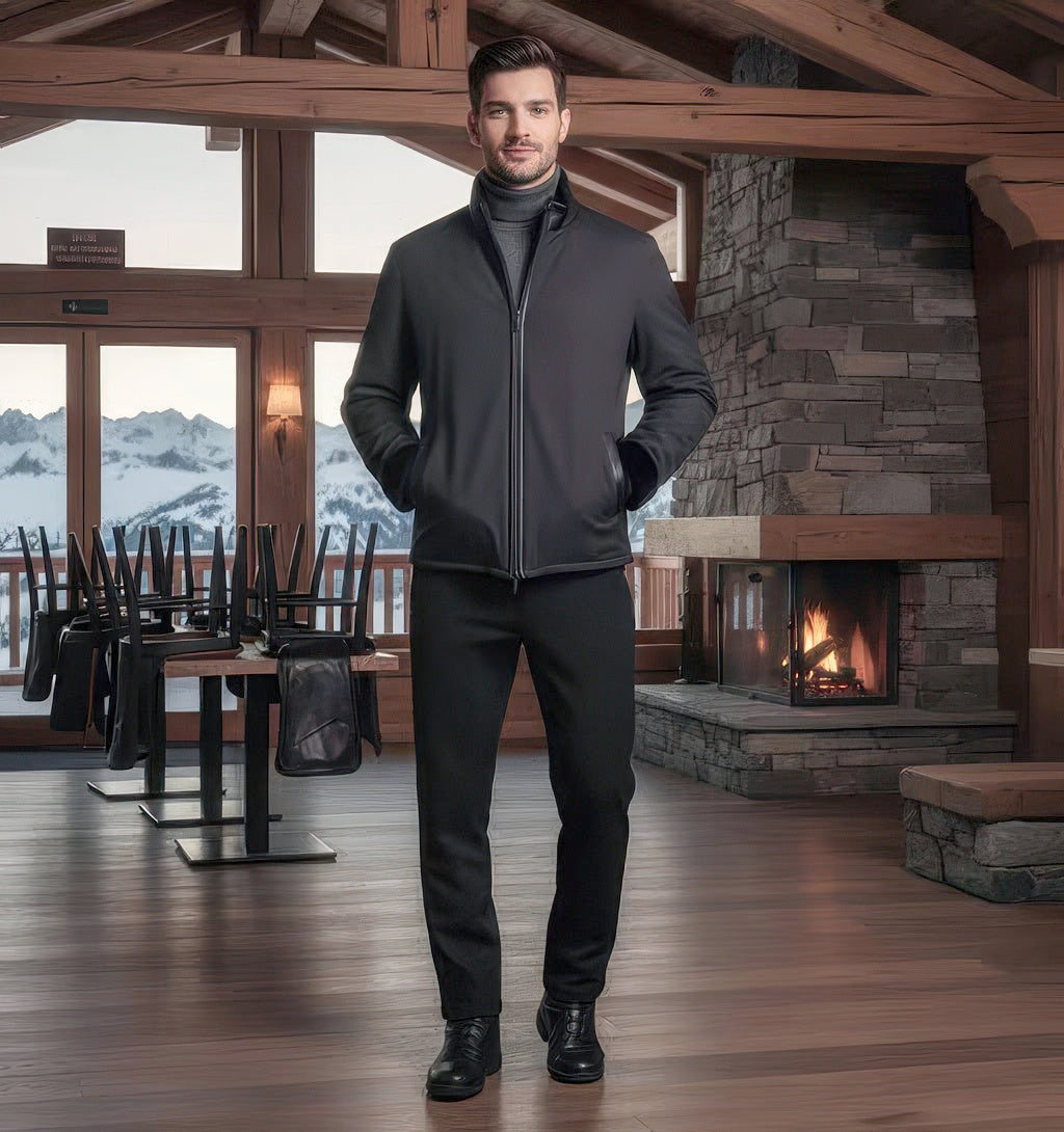 Man standing in an alpine lodge wearing the black shearling nylon zip jacket, stone fireplace and snowy mountains behind.