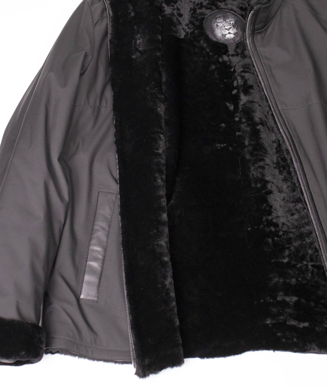 Close-up of the dark nylon jacket opened to show the plush black shearling lining and lion logo label.