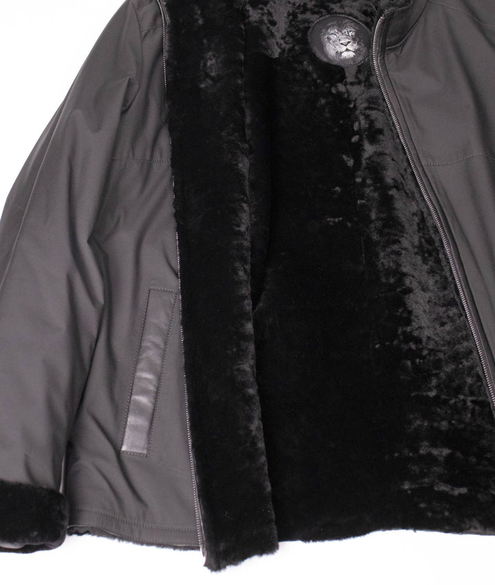 Close-up of the dark nylon jacket opened to show the plush black shearling lining and lion logo label.