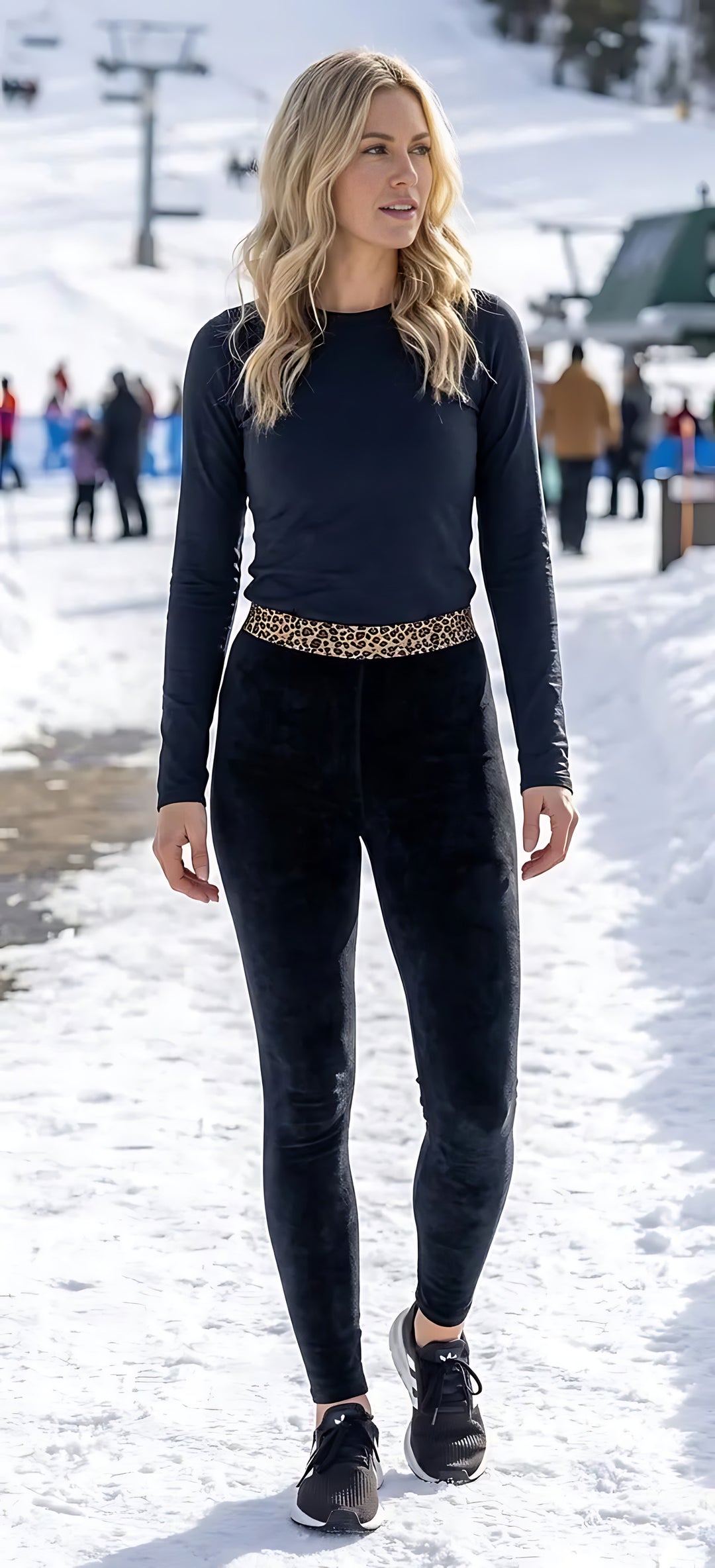 Woman walking at a snowy ski resort in navy velvet high-rise leggings with a leopard-print waistband, black long-sleeve top and sneakers.