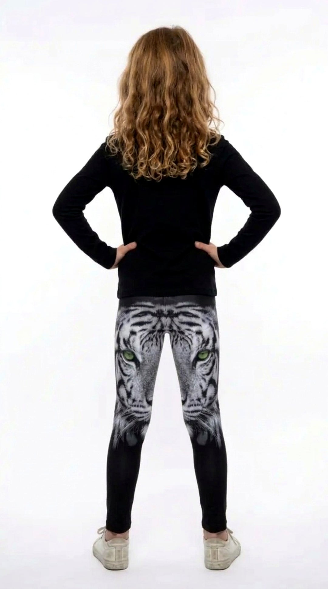 Back view of a girl with long curly hair wearing black girls leggings with a white tiger face on the upper legs