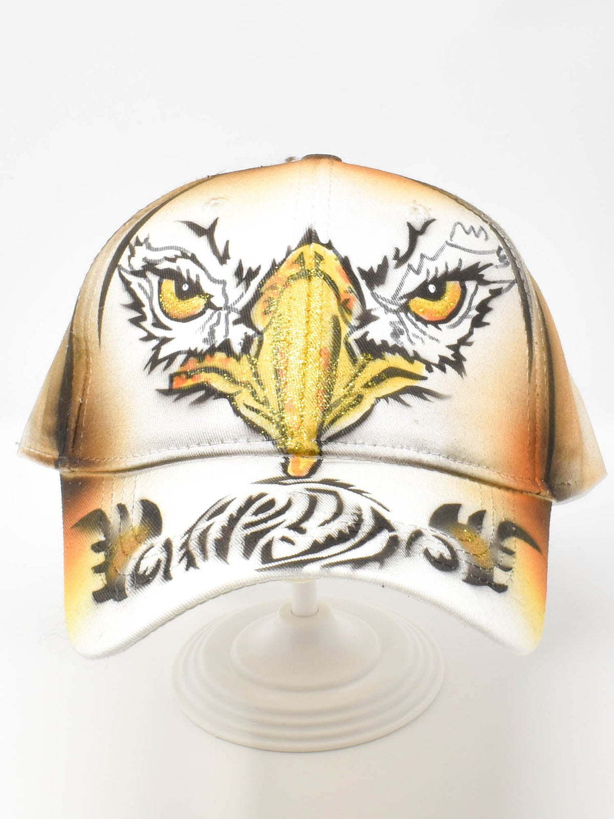 Hand painted eagle cap with an airbrushed eagle face and tribal brim artwork, front view on display stand.