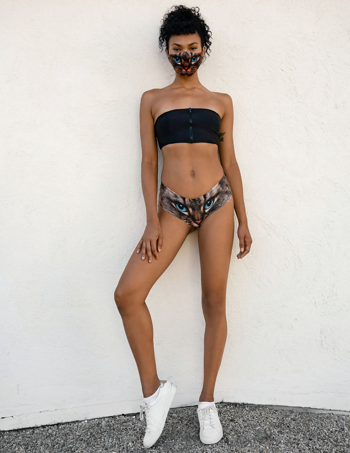 Full-length front view of woman wearing Green-Eyed Cat print panties, black strapless top, cat face mask, and white sneakers.