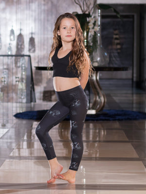 Young girl modeling kids Cane Corso Mastiff print leggings with a black sports bra, standing barefoot on a tiled floor indoors.